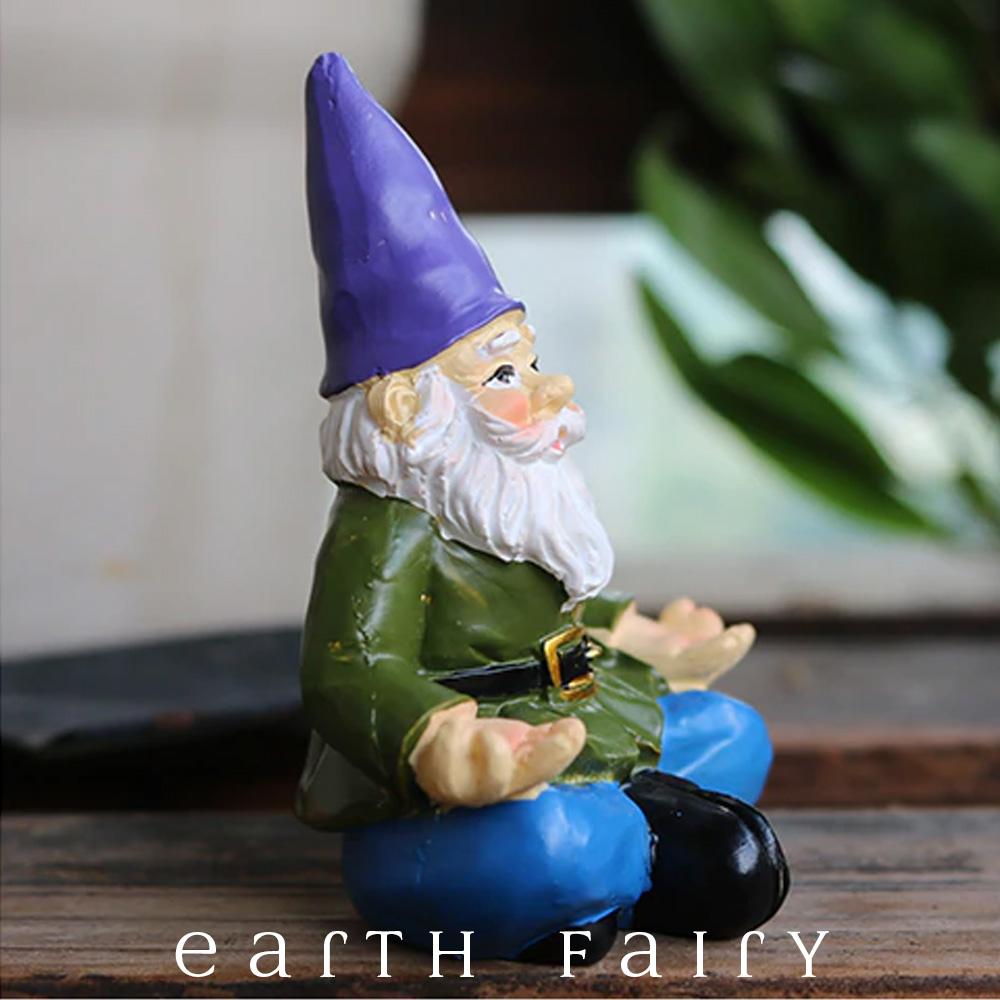 Yoga Gnome, wears blue pants and green belted coat with a purple hat and sits in a classic yoga pose